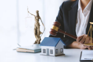 Lawyer holding gavel near model house and justice scale, symbolizing real estate law and property rights consultation.